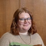 Photograph of a white female in her late thirties with medium length red hair. She is smiling and wearing a brown top.